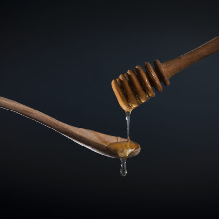 sweet Golden honey flows down a wooden stick on a wooden spoon on a dark background. Front view. Dark and mood photo